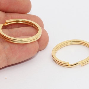 Puede incluir: Dos llaveros dorados con un diseño de doble banda. Los anillos son circulares con una ranura para sujetar las llaves. Los anillos se muestran sobre un fondo blanco.