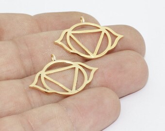 May include: Two gold-colored pendants in the shape of an eye with a geometric design. Each pendant features a circular frame with a triangle inside and petal-like shapes around the edges. The pendants have small loops at the top for attaching to a chain or other jewelry.