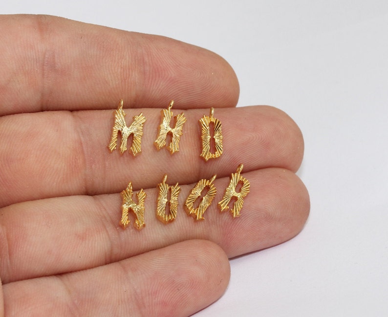 Puede incluir: Amuletos de alfabeto de metal dorado. Los amuletos tienen la forma de las letras M, H, B, H, O y A. Cada amuleto tiene un peque&ntilde;o lazo en la parte superior para sujetarlo a una cadena u otra joya. Las letras tienen un dise&ntilde;o de rayos de sol.