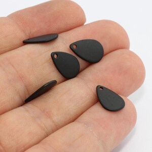 May include: A collection of matte black teardrop-shaped charms with small holes for jewelry making. The charms are in various sizes and orientations, showcasing their smooth, flat surfaces. Ideal for crafting earrings, necklaces, or other accessories.