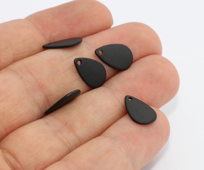 May include: A collection of matte black teardrop-shaped charms with small holes for jewelry making. The charms are in various sizes and orientations, showcasing their smooth, flat surfaces. Ideal for crafting earrings, necklaces, or other accessories.