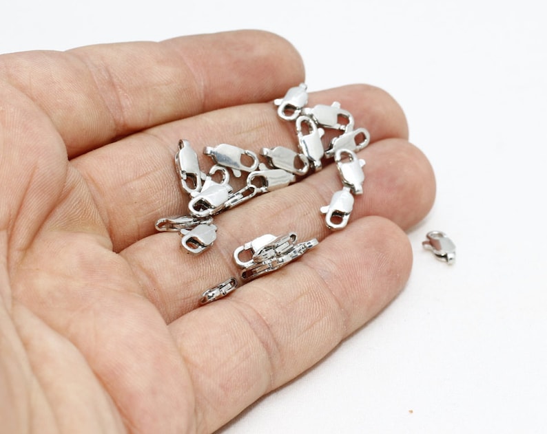 Pu&ograve; includere: Una collezione di piccole chiusure a moschettone in metallo color argento, ciascuna dotata di un meccanismo a molla e di un piccolo anello a un'estremit&agrave; per il fissaggio. Questi componenti per gioielli servono per fissare collane e bracciali.