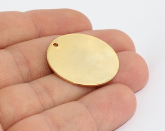 May include: A gold-colored, oval-shaped metal pendant with a small hole at the top for stringing. The pendant has a smooth, polished surface and is likely used for jewelry making or crafting.