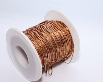 May include: A spool of copper-colored metallic thread. The thread is tightly wound around a white plastic spool. The metallic thread has a slight sparkle and is likely used for crafting or decorative purposes.