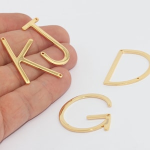 以下が含まれることがあります： 金色の金属製文字チャーム4つ：K、J、D、G。文字はシンプルなサンセリフ体で、ジュエリーやその他の工芸品に取り付けるための小さな穴があります。文字は光沢があり、反射します。