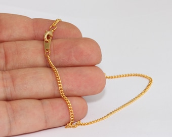 May include: A gold-colored chain necklace with a lobster clasp. The chain is made of small, interconnected links. The clasp is rectangular and has a small lever to open and close the necklace. The necklace is displayed against a white background.