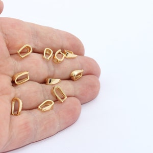 Puede incluir: Una colección de pequeñas presillas doradas para colgantes. Las presillas tienen varias formas, incluyendo diseños en forma de U y rectangulares. Probablemente se utilizan para la fabricación de joyas, con una superficie brillante y reflectante.