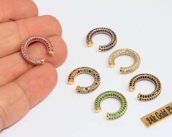 May include: Gold-plated ear cuffs with various coloured gemstones. One cuff is held in a hand, others are on a white surface. The cuffs feature pink, blue, clear, black, green, and multi-coloured stones. A small tag reads "24k Gold Plated."