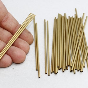 May include: A selection of small, gold-coloured metal tubes. Some are held in a hand, while others are scattered. The tubes appear to be hollow and have a consistent diameter. The image suggests a craft or jewellery-making supply.