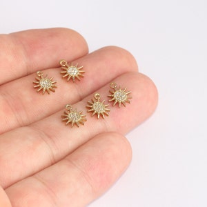 May include: Several small, gold-colored sun charms with a central circle of clear crystals and spiky rays extending outward. Each charm has a small loop at the top for attaching to jewelry. The charms are displayed against a light background.