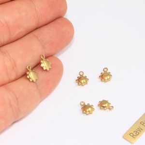 Könnte beinhalten: Mehrere kleine, goldfarbene Messinganhänger in Sonnenform werden auf weißem Hintergrund gezeigt. Die Anhänger haben oben eine Schlaufe zum Befestigen an Schmuck. Ein kleines Messingrechteck mit dem Text "Raw Brass" ist ebenfalls vorhanden.