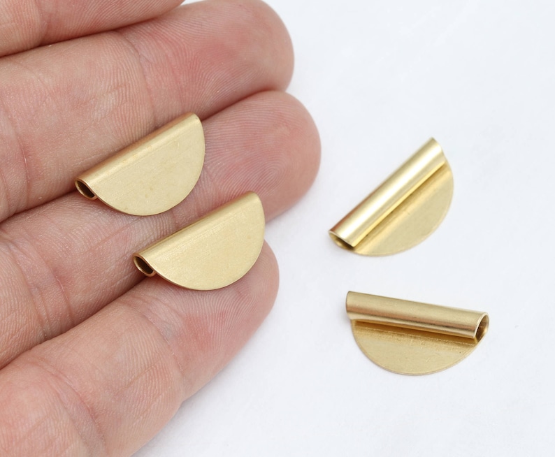 Puede incluir: Cuatro peque&ntilde;os componentes de joyer&iacute;a de metal de color dorado. Cada componente tiene forma de semic&iacute;rculo con un tubo cil&iacute;ndrico unido al borde recto. Los componentes se muestran sobre un fondo blanco.