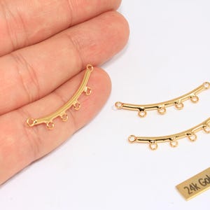 Puede incluir: Encantos conectores curvos chapados en oro con múltiples bucles para la fabricación de joyas. Los encantos son de color dorado brillante. Una pequeña etiqueta rectangular dice "24k Gold Plated".