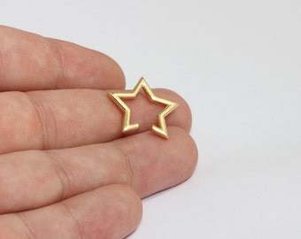 May include: A small, gold-coloured open-frame star charm. The star has five points and a hollow centre. The charm is held in a person's hand against a white background. This charm could be used for jewellery making or other crafts.