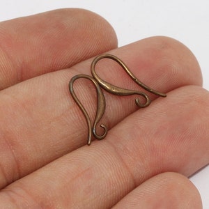 May include: Two antique copper-colored earring hooks. The hooks have a curved design with a looped bottom and a curved top. The earrings are displayed on a light background.