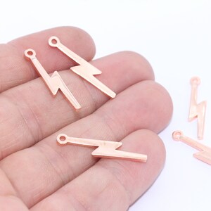 May include: Several small, rose gold-colored lightning bolt charms. Each charm has a small loop at the top for attaching to jewelry. The charms are displayed against a white background.