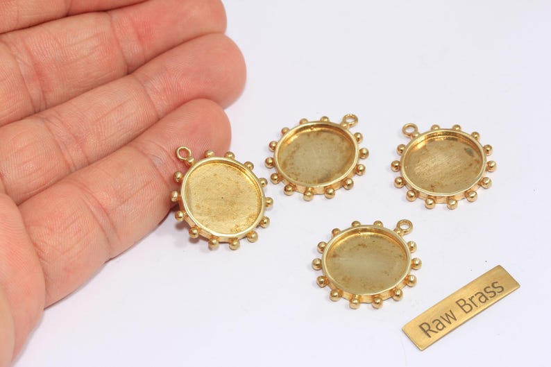 May include: Four brass pendant trays with a circular design and a small loop for attaching to a chain. Each tray has a raised edge with small, evenly spaced decorative balls. A small brass tag reads "Raw Brass."
