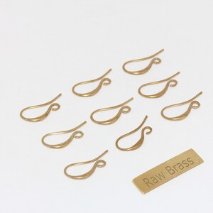 May include: Nine gold-coloured earring hooks are displayed on a white surface. A small rectangular brass tag with the text "Raw Brass" is also present. These hooks are suitable for jewellery making.