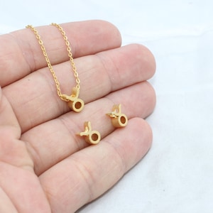 May include: Gold-colored Taurus zodiac symbol necklace and two matching charms. The necklace features a delicate chain. The charms and pendant are in the shape of the Taurus symbol. The jewelry is displayed on a white background.