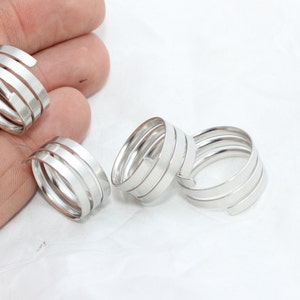 May include: Four silver-colored spiral rings. Each ring has a unique design with multiple bands that wrap around the finger. The rings are displayed on a white surface, showcasing their metallic sheen.
