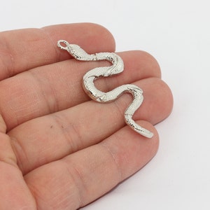 Peut inclure: Un charm en forme de serpent argenté avec une surface texturée. Le charme est en forme de serpent incurvé, avec une boucle en haut pour l'attacher à un collier ou un bracelet. Le corps du serpent est détaillé avec des écailles.