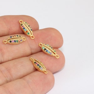 May include: Four gold-colored, oval-shaped jewelry connectors. Each connector is adorned with a row of colorful gemstones, including red, blue, green, and yellow. The connectors have small loops on each end for attachment.