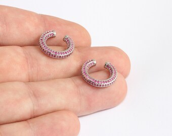 May include: Two silver ear cuffs, each in a C-shape, are shown. They are adorned with small, bright pink gemstones. The design is simple but elegant, with the gemstones providing a splash of colour and sparkle to the ear cuffs.