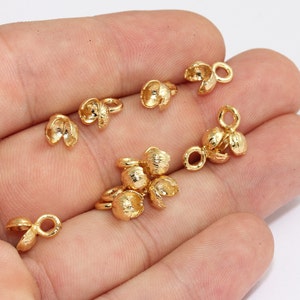 May include: A collection of small, gold-colored jewelry findings, including flower-shaped bead caps and components with loops for attaching to other jewelry pieces. The findings are made of a shiny, metallic material.