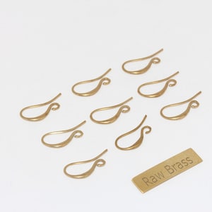 Peut inclure: Présentation de neuf crochets de boucles d'oreilles dorés sur une surface blanche. Une petite étiquette rectangulaire en laiton avec le texte "Raw Brass" est également présente. Idéal pour la création de bijoux.