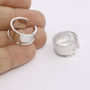 May include: Two silver-colored ear cuffs. Each cuff has a curved design with a flat, rectangular center and a rounded edge. The cuffs are shown against a white background.