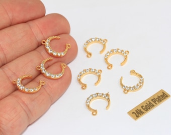 Puede incluir: Varios dijes en forma de media luna dorada con cristales transparentes incrustados a lo largo del borde curvo. Cada dije tiene dos pequeños bucles en los extremos. Una etiqueta rectangular dorada muestra el texto 24k Gold Plated.