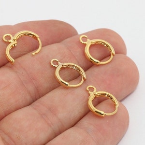 May include: Several gold-colored earring findings are displayed against a white background. The findings are small, hoop-shaped, and have a hinged design for easy attachment. Each finding has a small loop for attaching a charm or other decorative element.