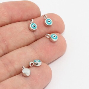 May include: Small, silver-colored charm pendants with a turquoise blue enamel eye design and a small loop for attaching to jewelry. The eye has a black pupil. The charms are round and have a polished finish.