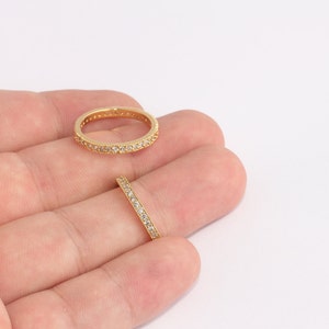 Puede incluir: Dos anillos dorados con pequeñas piedras preciosas transparentes. Un anillo es totalmente visible, el otro parcialmente. Los anillos están sobre un fondo blanco. Los anillos son probablemente para joyería o moda.