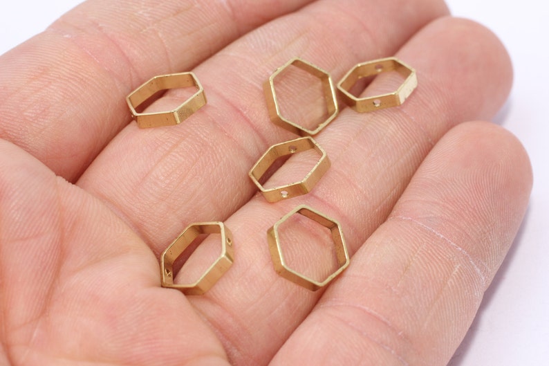 May include: Several small, gold-colored, hexagonal metal charms. Each charm has a hollow center and small holes for stringing. The charms are displayed against a neutral background.