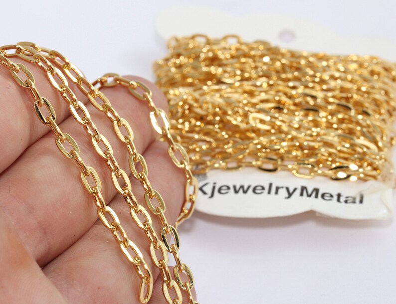 May include: Close-up of a gold-colored chain with oval links. The chain is in a roll and also laid out in a line. The chain is shiny and appears to be new. The text "KjewelryMetal" is visible on the packaging.