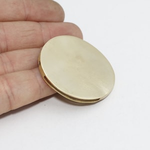 May include: A gold-colored, oval-shaped metal object with a brushed finish. The object has a flat top and a slightly curved edge with a recessed channel. There are small holes on the side. The object is likely a component or decorative element.
