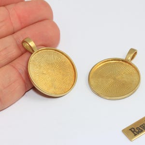 Puede incluir: Dos bandejas de colgante de latón dorado, una ovalada y otra redonda, con un lazo para una cadena. Las bandejas tienen una superficie texturizada. También hay un pequeño rectángulo de latón con el texto "Raw Brass".