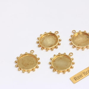 May include: Four gold-coloured brass bezel trays with a circular design and a small loop for hanging. The trays have a raised edge with small, evenly spaced decorative balls. A small brass tag reads "Raw Brass."