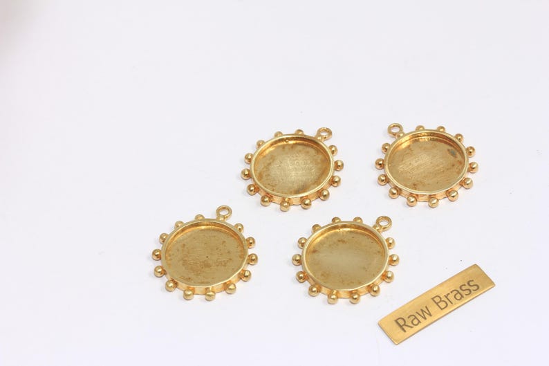 May include: Four gold-coloured brass bezel trays with a circular design and a small loop for hanging. The trays have a raised edge with small, evenly spaced decorative balls. A small brass tag reads "Raw Brass."