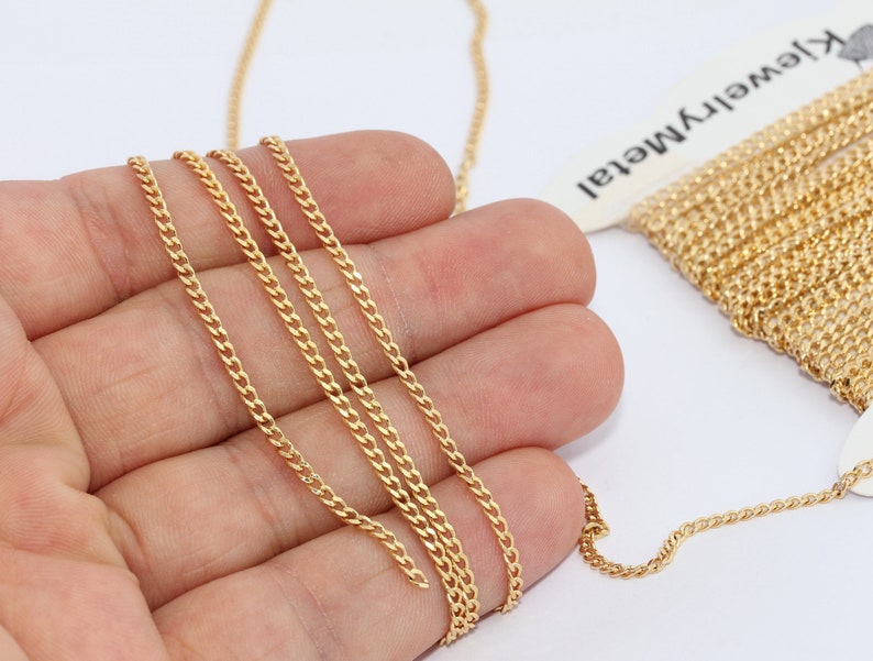 Puede incluir: Primer plano de una cadena de oro, sostenida en una mano, con un carrete de cadena en el fondo. La cadena tiene un acabado met&aacute;lico brillante. La cadena se utiliza probablemente para la fabricaci&oacute;n de joyas y se muestra sobre un fondo blanco.