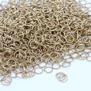 Könnte beinhalten: Ein Haufen kleiner, goldfarbener Sprungringe. Diese offenen Ringe werden für die Schmuckherstellung und andere Bastelarbeiten verwendet. Die Ringe sind rund und haben eine kleine Öffnung zum Verbinden anderer Komponenten. Die Ringe sind aus Metall.