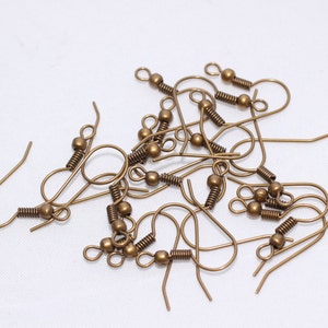 May include: A collection of antique bronze-colored earring hooks. Each hook features a curved wire, a coiled spring, and a decorative bead. These components are designed for jewelry making and crafting projects.