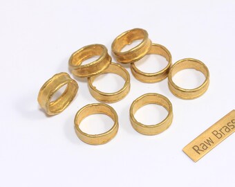 May include: A collection of eight raw brass rings with a golden hue, displayed on a white surface. The rings vary slightly in shape and texture. A small brass rectangle with the text "Raw Brass" is also present.