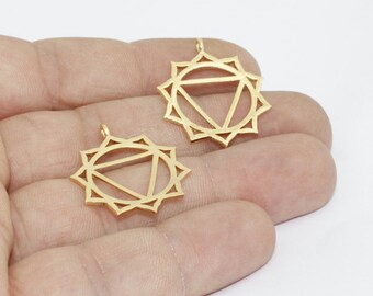 May include: Two gold-colored pendants with a sunburst design and a triangle in the center. The pendants are held in a hand against a white background. The pendants are likely for jewelry making or crafting.