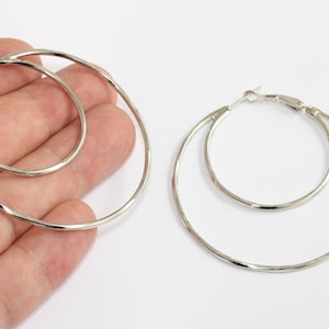 Pode incluir: Brincos de argola duplos prateados. Os brincos apresentam um aro externo maior e um aro interno menor, criando um efeito em camadas. Os aros têm um acabamento liso e polido e um fecho articulado.
