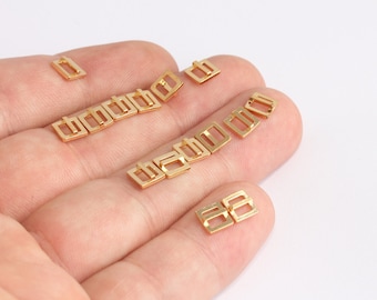 May include: A collection of small, gold-colored rectangular metal buckles. The buckles have a simple, minimalist design with a rectangular frame and a central bar. They are scattered on a white surface.