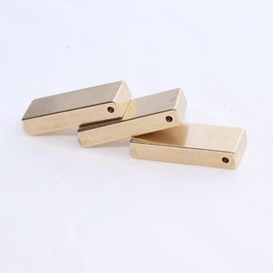 May include: Four rectangular, gold-colored metal hinges are arranged on a white surface. Each hinge has a small hole on one end. The hinges are slightly angled, suggesting they are connected or can be joined.