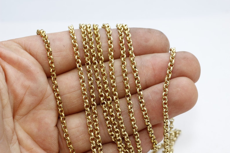 May include: Close-up of several strands of gold-colored chain. The chains are made of small, round links, creating a delicate and intricate pattern. The chains are held in a hand against a white background. The chains are likely for jewelry making.