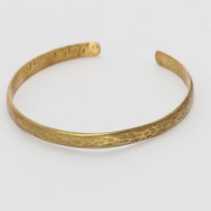 Puede incluir: Un brazalete de lat&oacute;n martillado. El brazalete abierto tiene una superficie texturizada y un color dorado c&aacute;lido. El brazalete es un dise&ntilde;o simple y elegante, adecuado para el uso diario.